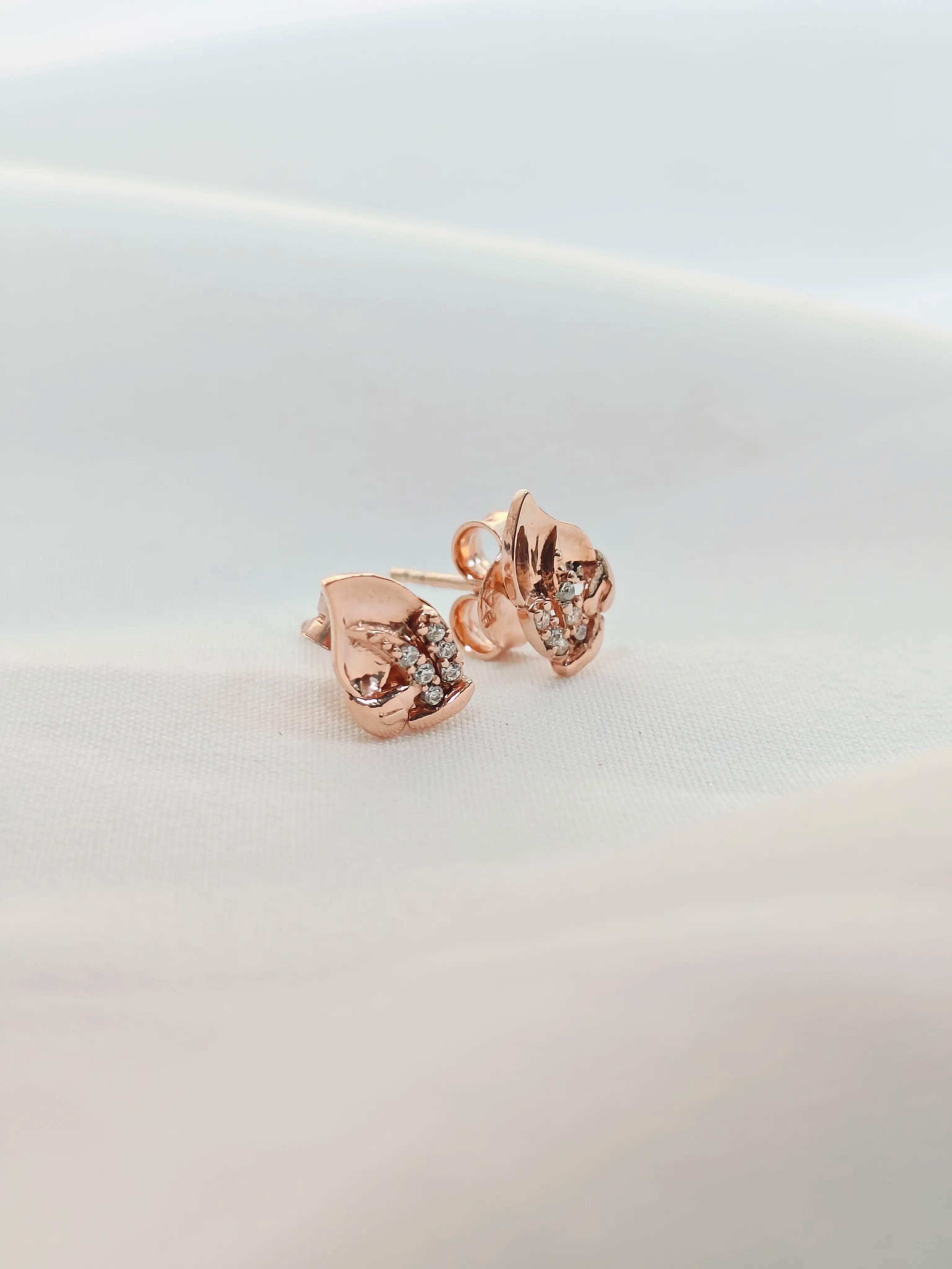 Rose gold earrings with clear gemstones on a light gray background